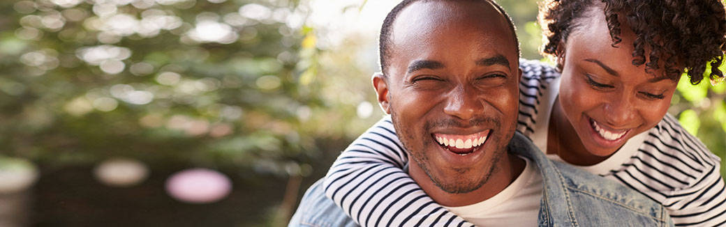 Smiling woman standing behind smiling man with her arms around his neck.