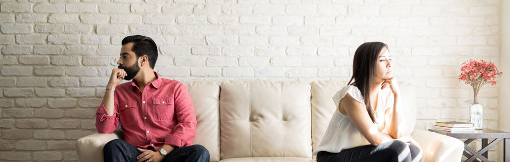 man and woman sitting on opposite ends of the couch, facing away from each other.